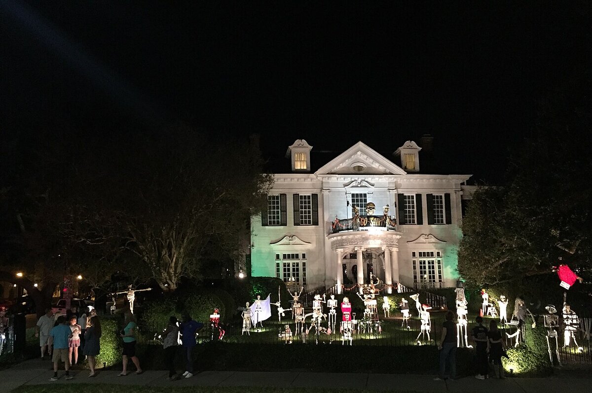 A house decorated with lit-up skeletons for Halloween at night, with visitors on the sidewalk