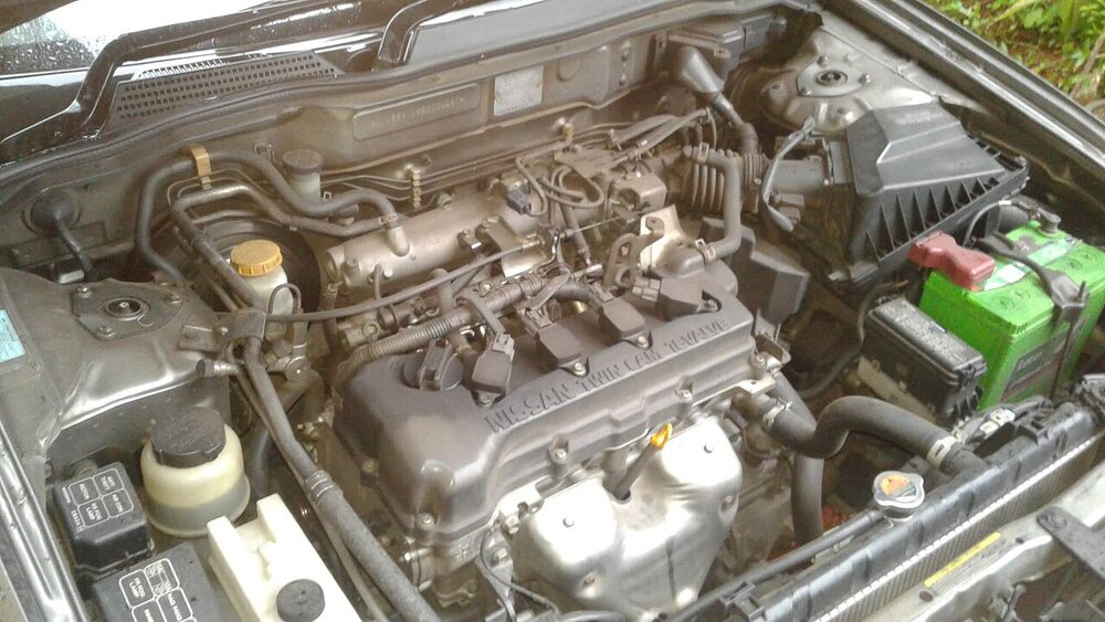Open car engine bay showing wiring, hoses and the battery