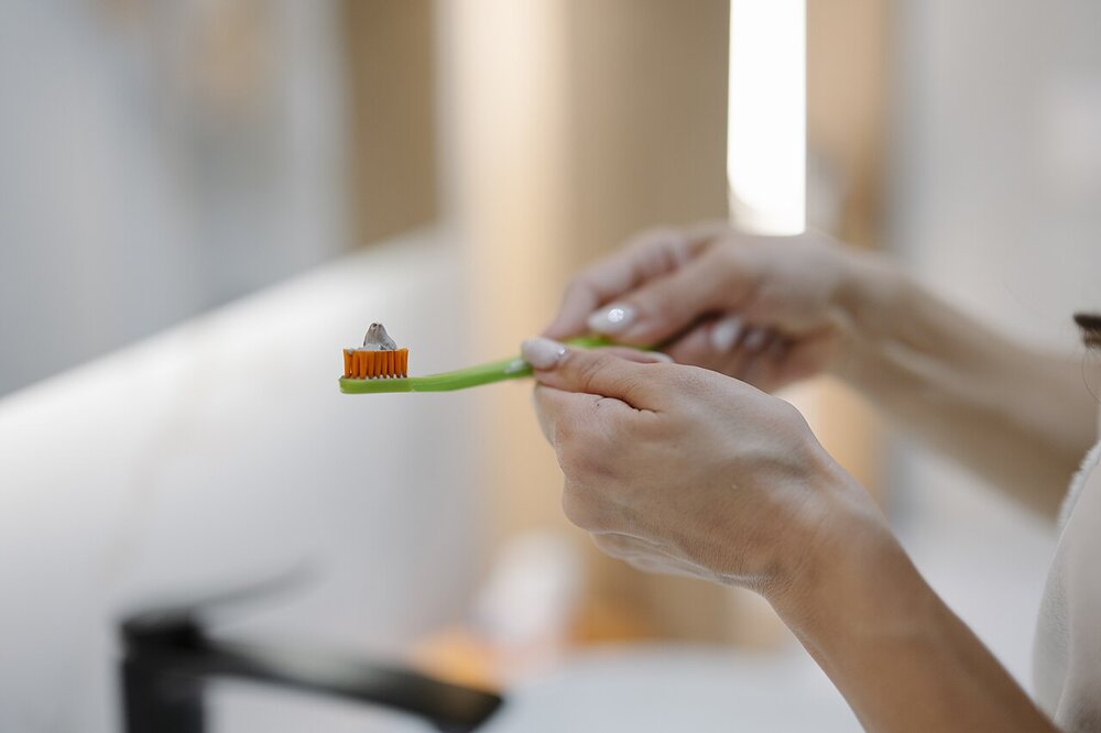 Person at a bathroom sink holding a toothbrush with toothpaste